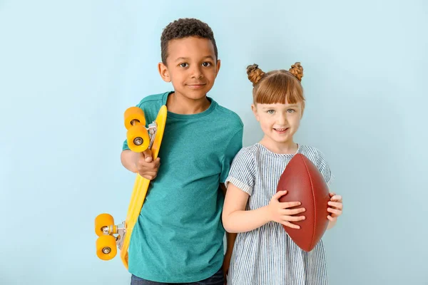 Cute little children with skateboard and rugby ball on color background — Stock Photo, Image