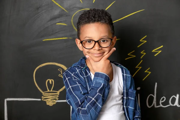 Thoughtful African-American boy near drawn light bulb on dark wall — Stock Photo, Image