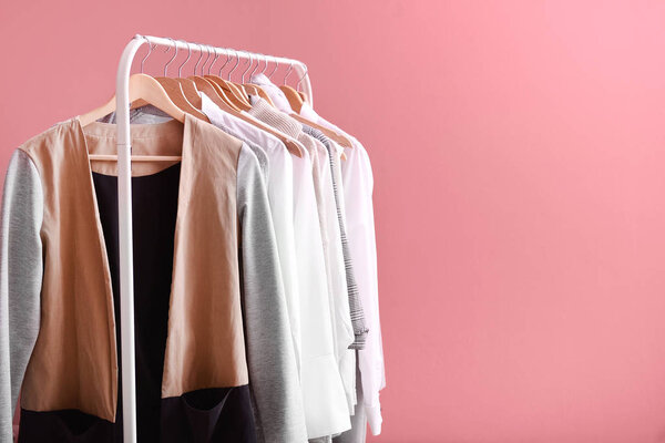 Стойка со стильной одеждой на цветном фоне