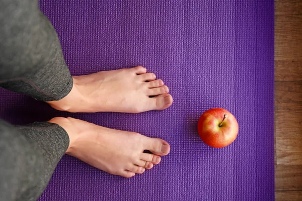 Benen van sportieve vrouw met appel op yoga mat — Stockfoto