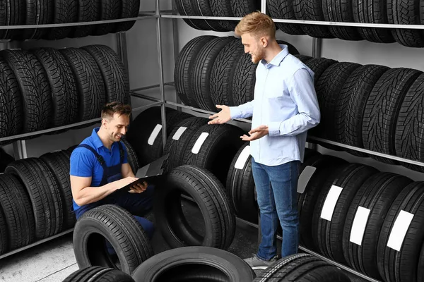 Säljaren hjälper man att välja däck i bil affär — Stockfoto