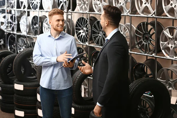 Seller helping man to choose disks and tires in car store