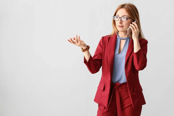 Portrait of mature businesswoman talking by phone on light background — Stock Photo, Image