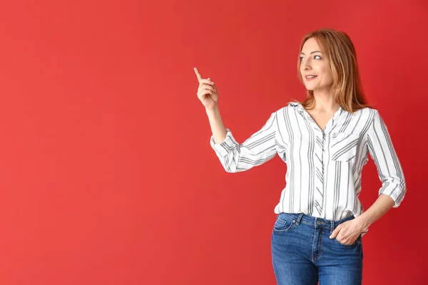 Portrait of mature woman pointing at something on color background — Stock Photo, Image
