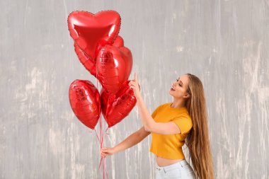 Beautiful young woman with heart-shaped air balloons against grunge wall