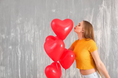 Beautiful young woman with heart-shaped air balloons against grunge wall