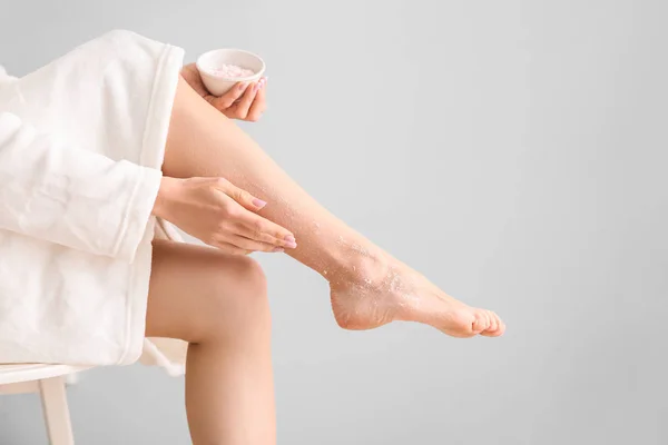 Young woman applying body scrub on legs against light background — Stock Photo, Image