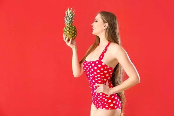 Yüzme takım elbiseli ve renkli arka planda ananas ile güzel genç kadın — Stok fotoğraf