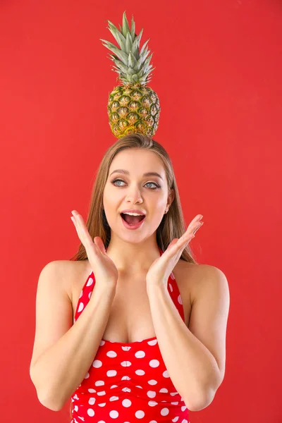 Surprised young woman in swimming suit and with pineapple on color background