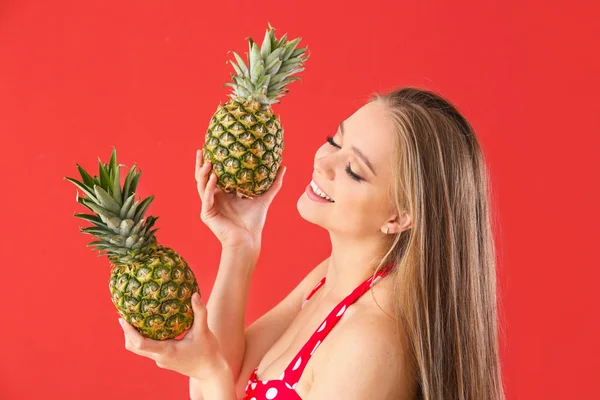 Beautiful young woman in swimming suit and with pineapples on color background — Stock Photo, Image