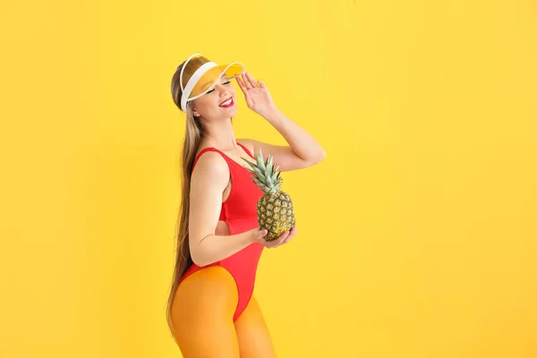 Beautiful young woman in swimming suit, tights and with pineapple on color background — Stock Photo, Image