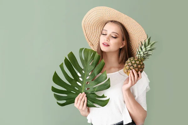 Mooie jonge vrouw met ananas en tropische blad op kleur achtergrond — Stockfoto