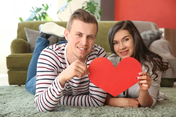 Happy young couple with paper heart at home — Stock Photo, Image