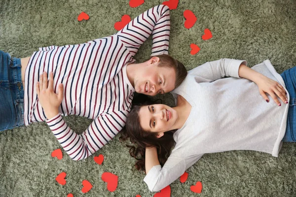 Feliz pareja joven con corazones de papel acostados en la alfombra — Foto de Stock