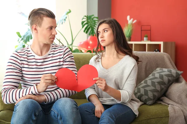 Unhappy young couple tearing apart paper heart at home. Conflict in relationship — Stock Photo, Image