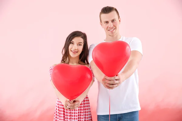 Glückliches junges Paar mit Luftballons auf farbigem Hintergrund — Stockfoto