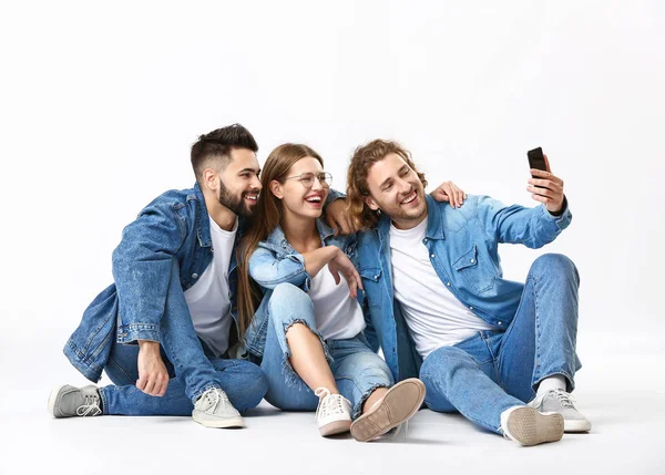 Elegantes jóvenes en ropa vaquera tomando selfie sobre fondo blanco — Foto de Stock