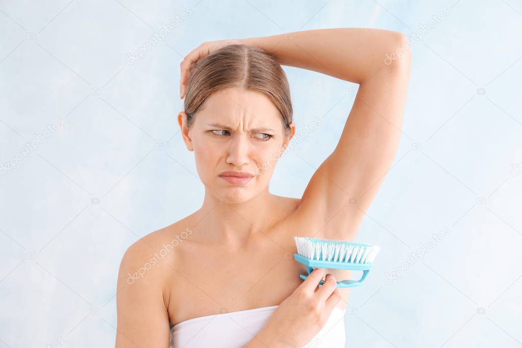 Displeased young woman with cleaning brush on light background. Depilation concept