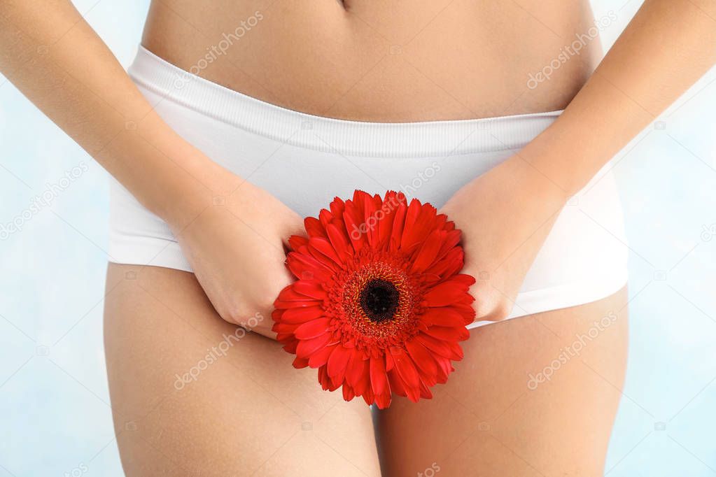 Beautiful young woman in underwear and with flower on light background