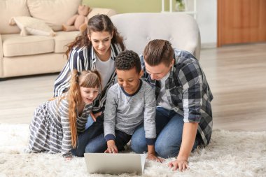 Evde dizüstü bilgisayar kullanan küçük evlatlık çocukları ile Mutlu çift