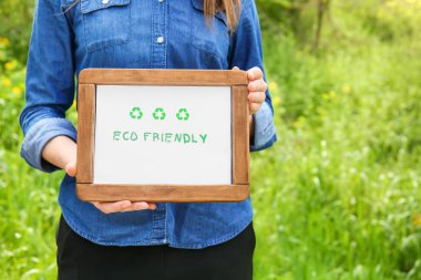 Açık havada Eco Friendly yazan bir pano tutan kadın.