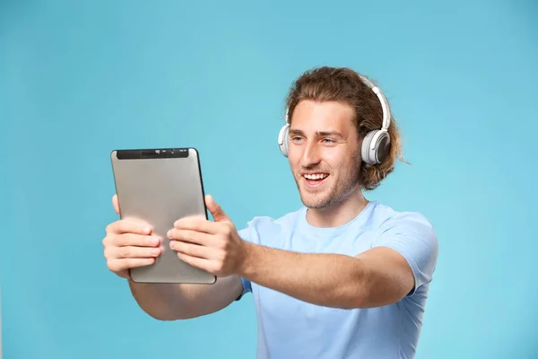 Handsome man with tablet computer and headphones on color background — Stock Photo, Image