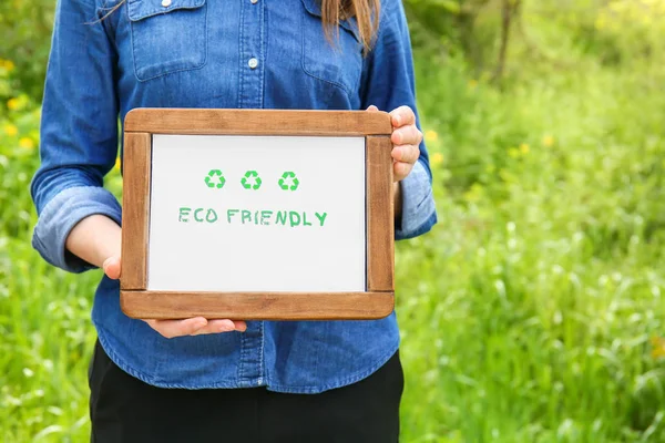 Woman holding board with text ECO FRIENDLY outdoors