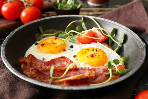 Frying pan with tasty eggs, bacon and tomato on table — Stock Photo, Image