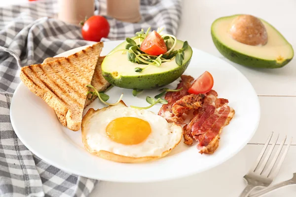 Plate with tasty fried egg, bacon, avocado and toasts on table — Stock Photo, Image