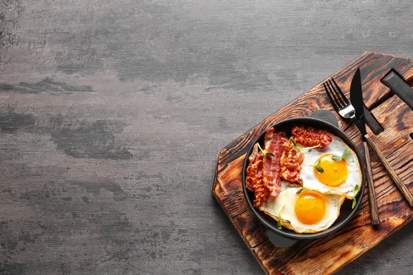 Frying pan with tasty eggs and bacon on grey background — Stock Photo, Image