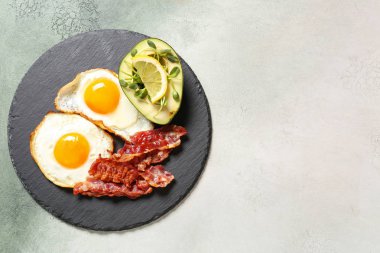 Hafif arka planda lezzetli kızarmış yumurta, pastırma ve avokado ile arduvaz plaka