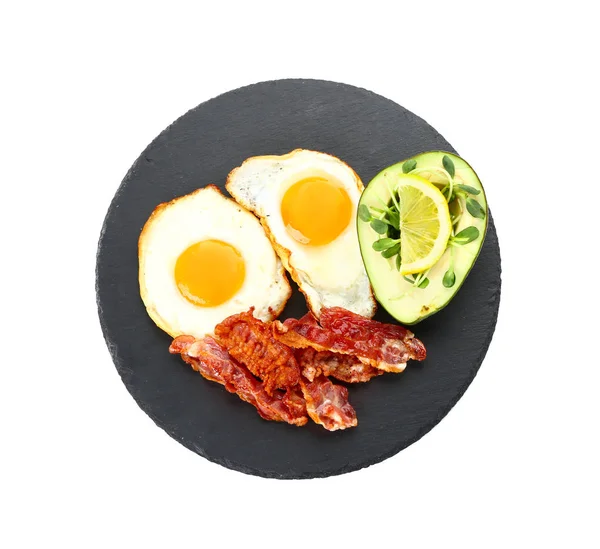 Slate plate with tasty fried eggs, bacon and avocado on white background — Stock Photo, Image