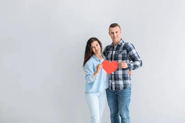 Adorable loving couple with paper heart on grey background — Stock Photo, Image