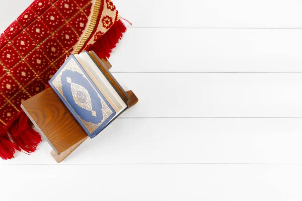 Muslim prayer mat and Koran on white wooden table