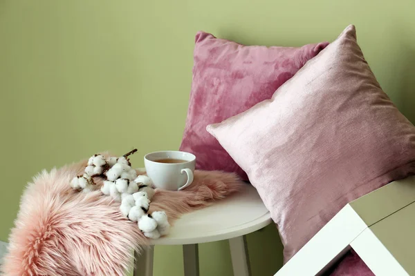 Table with cup of tea and soft pillows on color background — Stock Photo, Image