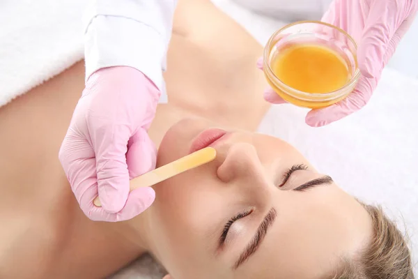 Beautician removing hair above upper lip of young woman in salon