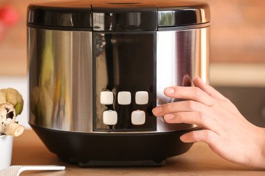 Woman switching on modern multi cooker on table, closeup