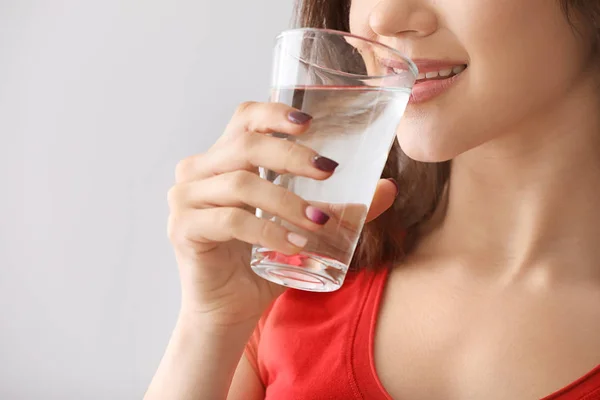 Beautiful young woman drinking water on light background, closeup — Stock Photo, Image