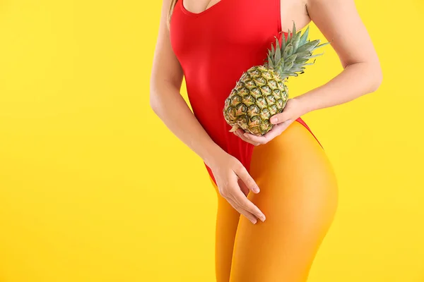 Mooie jonge vrouw in zwempak en met ananas op kleur achtergrond — Stockfoto