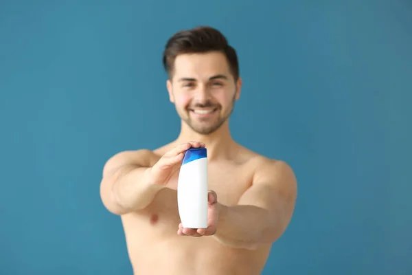 Bello uomo con bottiglia di shampoo su sfondo di colore — Foto Stock