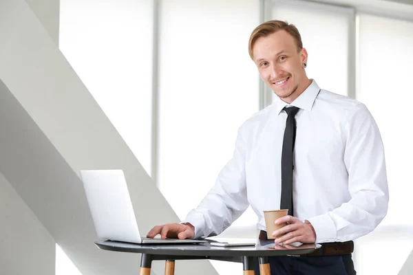 Handsome businessman with laptop drinking coffee in office — Stock Photo, Image