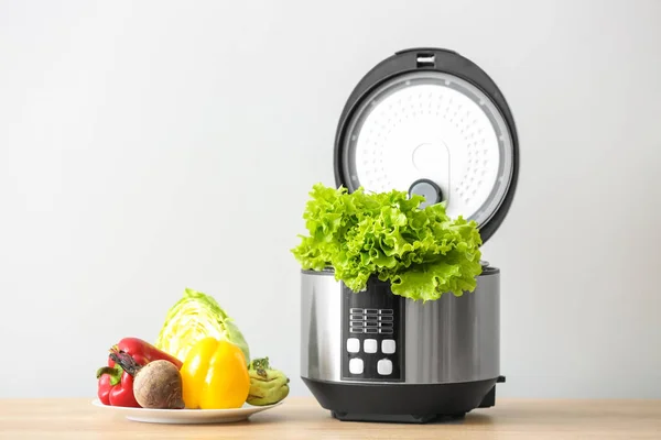 Modern multi cooker with vegetables on table against light background — Stock Photo, Image