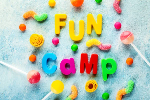 Words FUN CAMP and sweets on color background — Stock Photo, Image