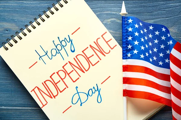 Notebook with text HAPPY INDEPENDENCE DAY and USA flag on color wooden background — Stock Photo, Image