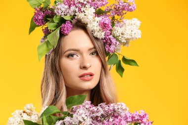 Beautiful young woman with lilac flowers on color background