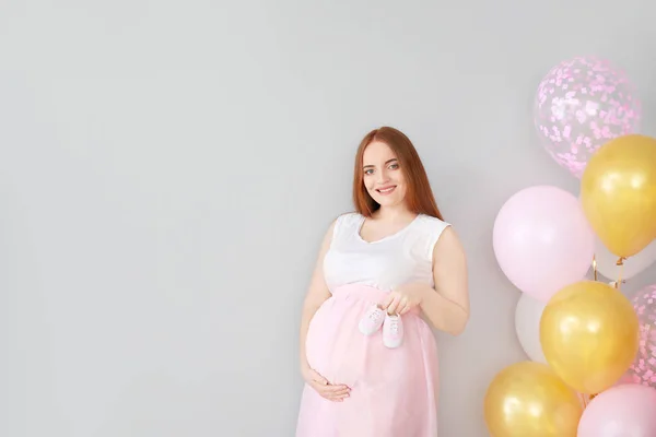 Beautiful pregnant woman with baby booties and balloons on light background — Stock Photo, Image