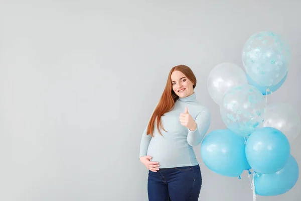 Hermosa mujer embarazada con globos mostrando el pulgar hacia arriba sobre fondo claro — Foto de Stock