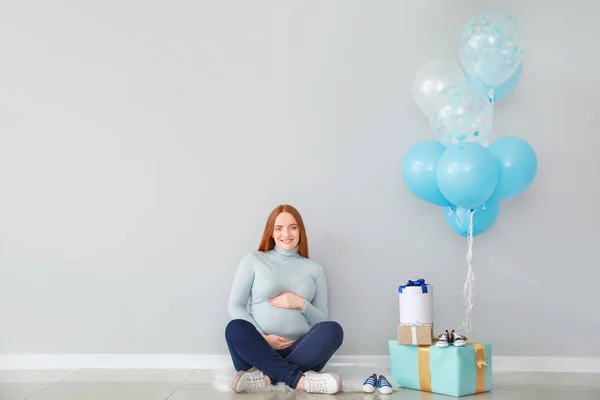 Belle femme enceinte avec des cadeaux de douche bébé près du mur de lumière — Photo