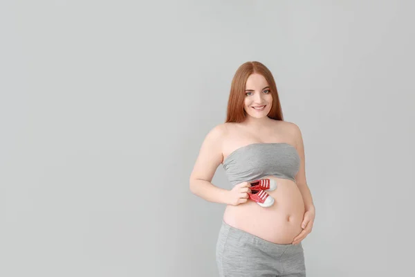 Mulher grávida bonita com botas de bebê no fundo claro — Fotografia de Stock