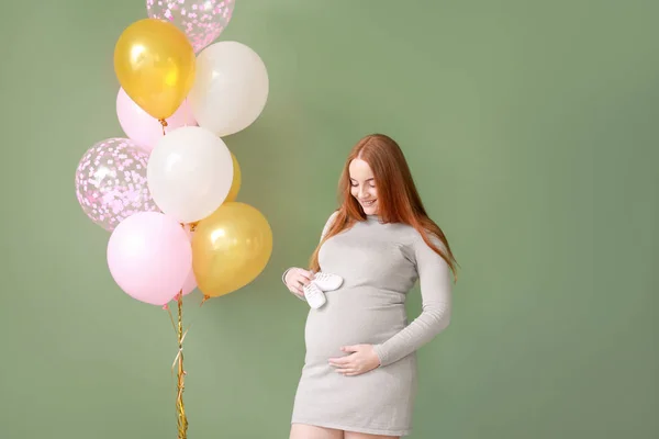 Hermosa mujer embarazada con botines de bebé y globos de aire sobre fondo de color — Foto de Stock